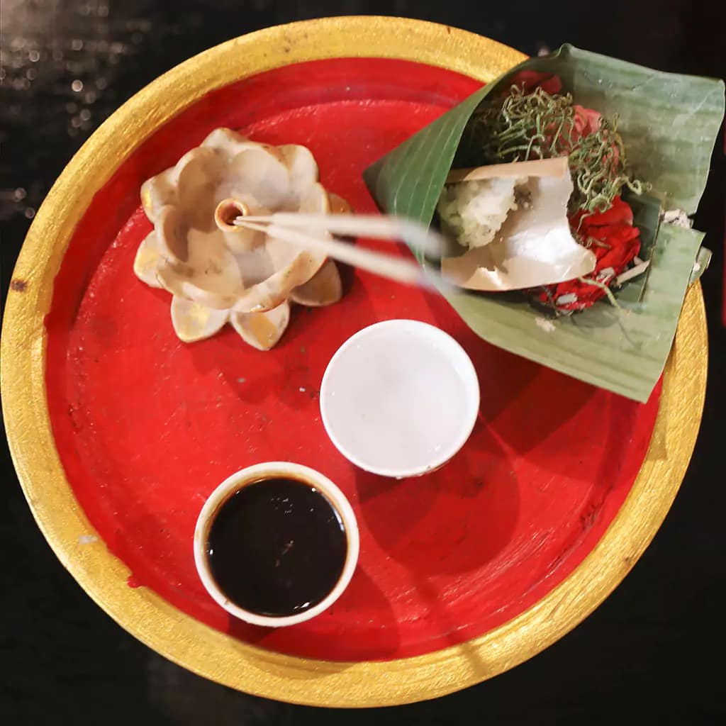 photo of bali offerings where canang sari, coffee, incense and tea are seen on a tray 