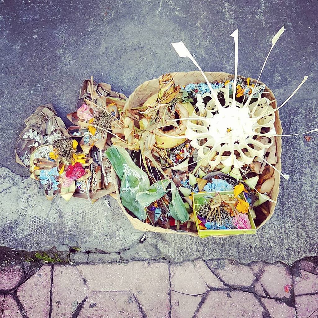 Photo of Balinese Pejati placed at the entrance to the house. visible piles of canang sari and oranges, bananas and other fruits in a knitted basket - bali hindu offerings