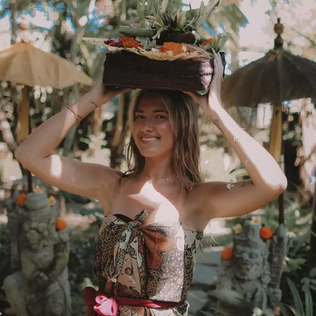 A female foreign tourist carrying a Balinese 'canang sari' offering while wearing traditional sarong, exploring cultural traditions in Bali. - religion of bali Indonesia