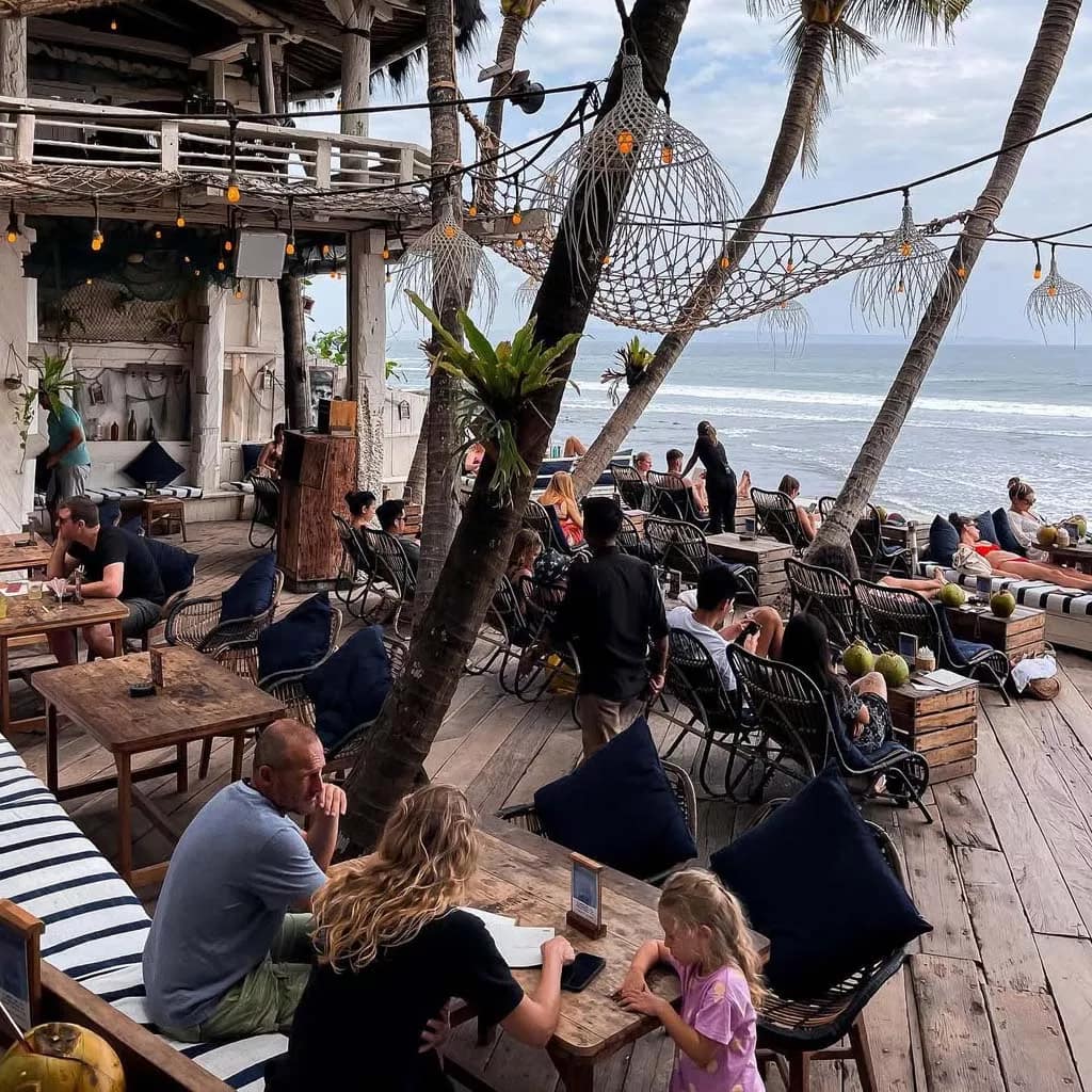 Beachfront café in Canggu, Bali with people enjoying food and ocean views — a popular stop after traveling from Bali Airport to Canggu.