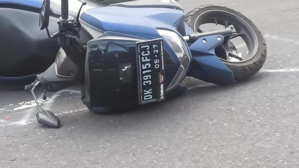 Crashed rental scooter lying on Bali road after accident - police negotiation scene for traffic violations