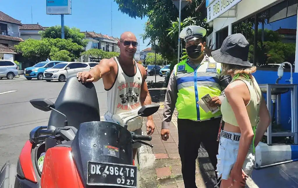 Police officer discussing with tourists during traffic stop in Bali - lighthearted moment of scooter law enforcement"