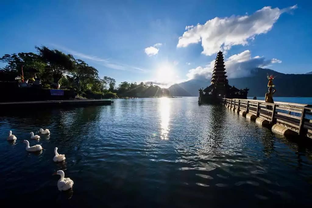 
landscape photo of batur temple and Balinese woman carrying offerings walking on the bridge to the temple with view of Lake Batur In bali