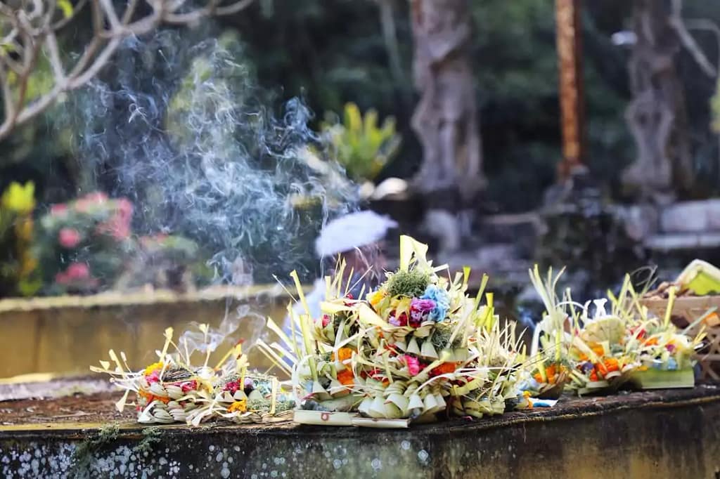 photo of a collection of canang sari in a sacred temple with incense burning and smoke rising to the top makes the meaning of the offering so deep. - bali hindu offerings