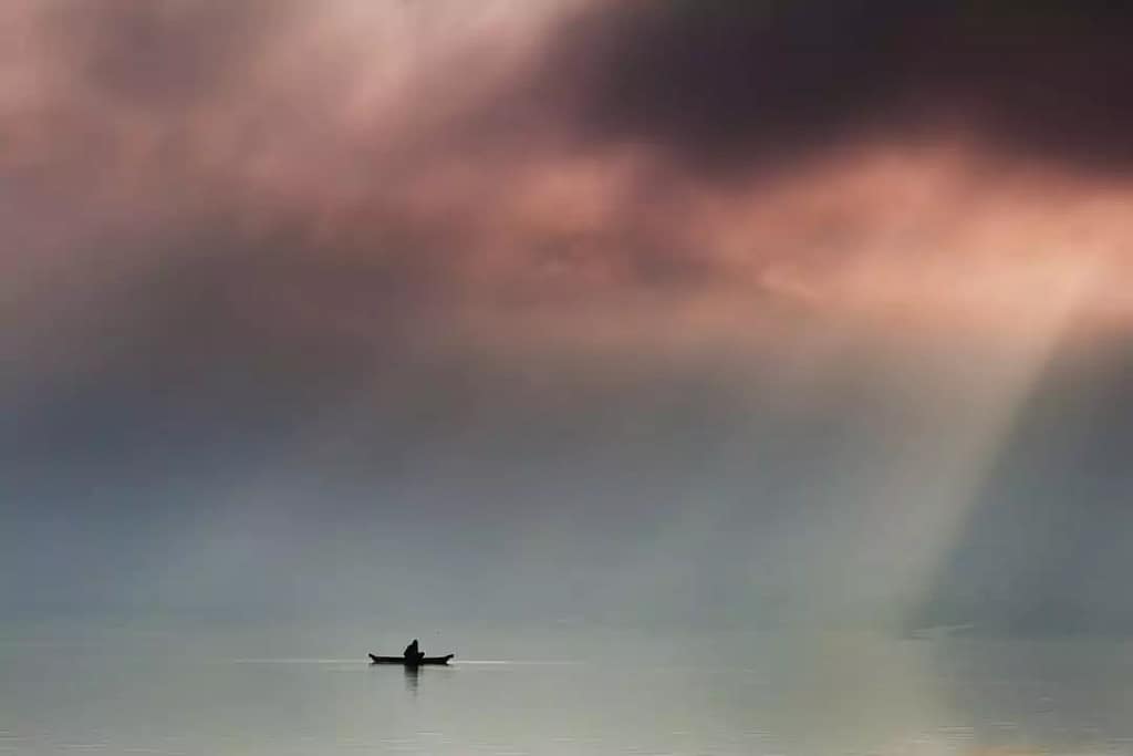 landscape photo of lake batur in bali, a fisherman on a traditional boat in the morning with sunlight penetrating through thick clouds..very beautiful