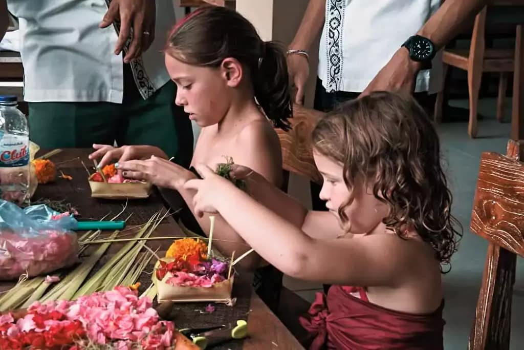 2 Caucasian girls aged 5 and 3 years old are busy arranging and making canang sari wearing sarongs 