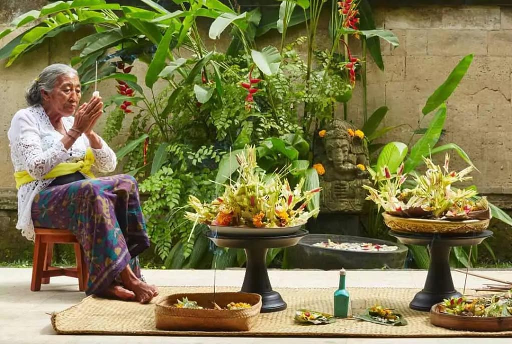 A close-up of two hands holding Canang Sari, traditional Balinese Hindu offerings made from woven palm leaves, colorful flowers, and natural elements. These offerings are part of daily rituals in the religion of Bali, Indonesia, symbolizing gratitude and spiritual balance.