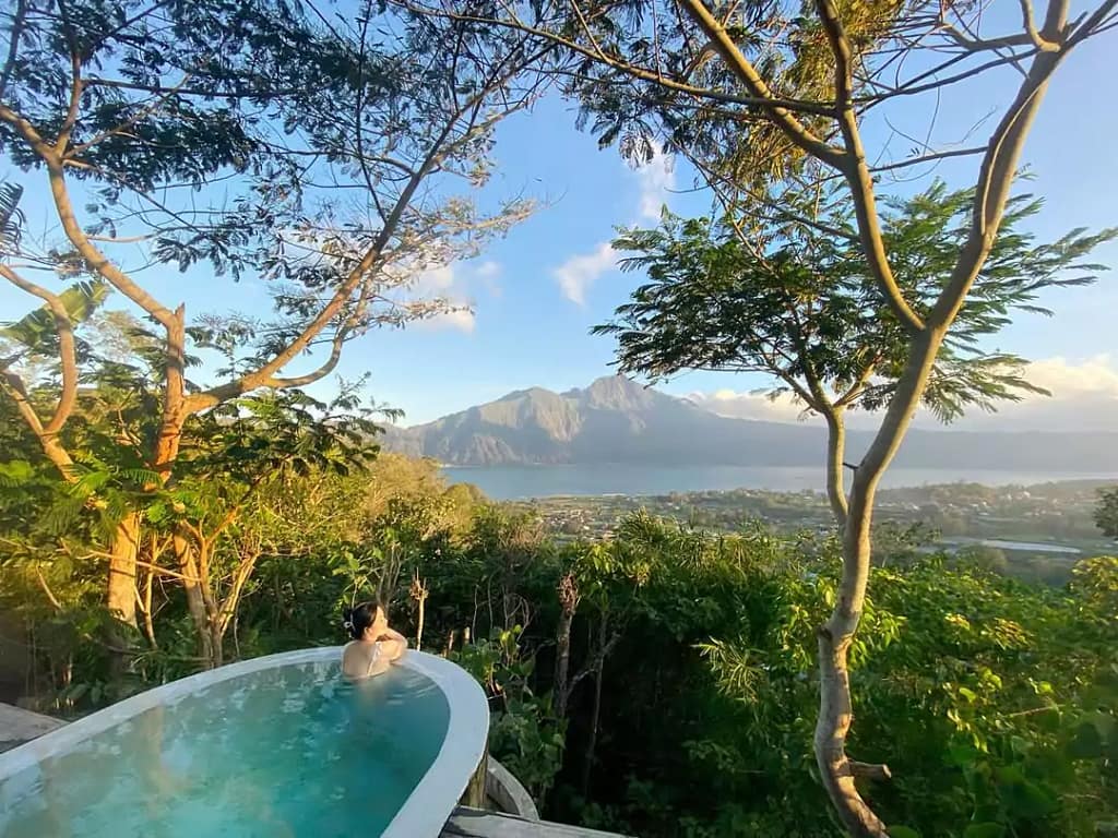 photo of a woman soaking in the pool and enjoying the beautiful view of forest, mountain and lake batur in the morning