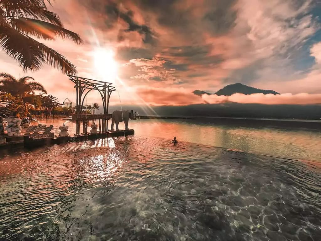 A beautiful sunset view of a woman soaking in a hot spring pool in kintamani, with mountains and Lake Batur in the background.