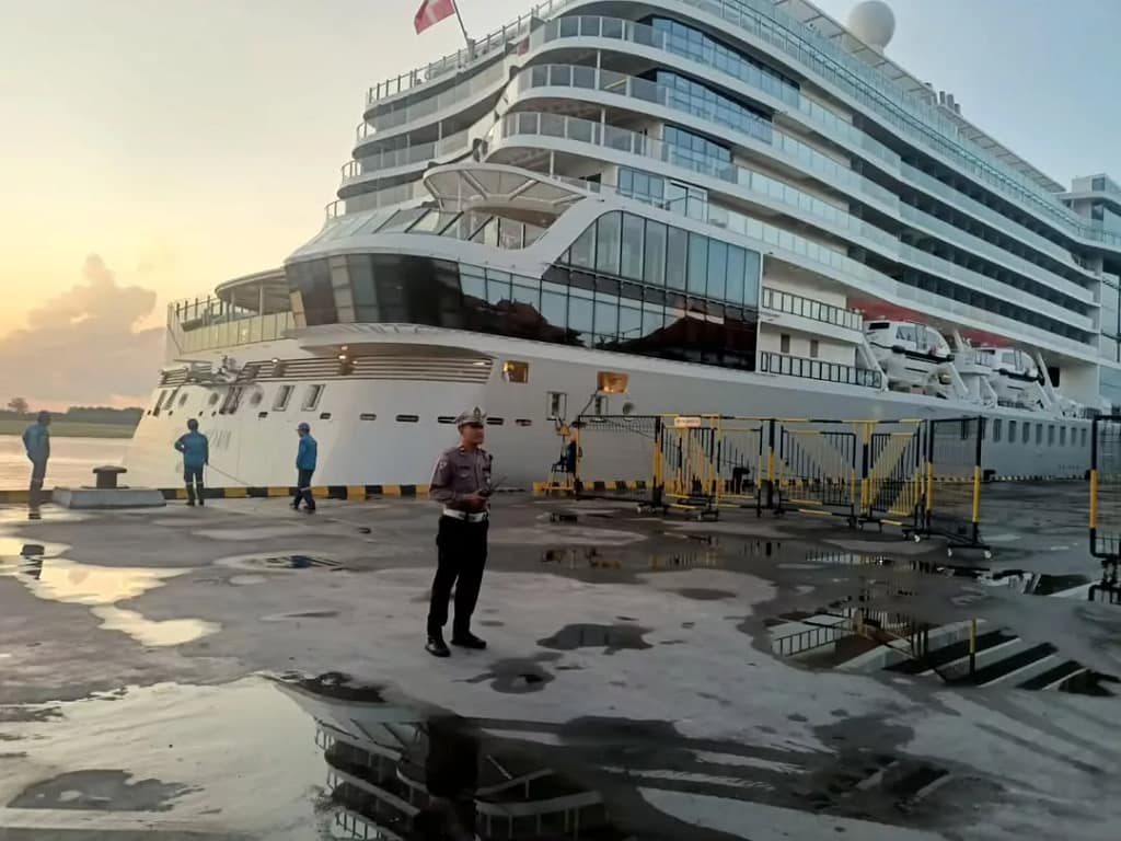 A large cruise ship docked at Benoa Port at sunset, with a security officer overseeing operations, illustrating the arrival point for thousands of travelers seeking transfers.