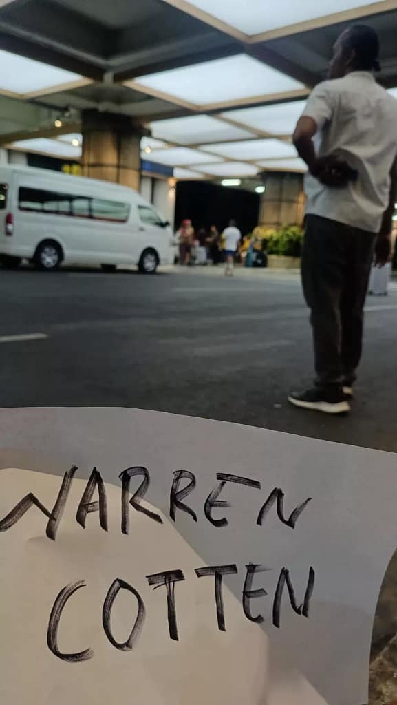 photo of an online travel agent driver waiting for guests at Bali airport while holding a piece of paper with the guest's name written on it
