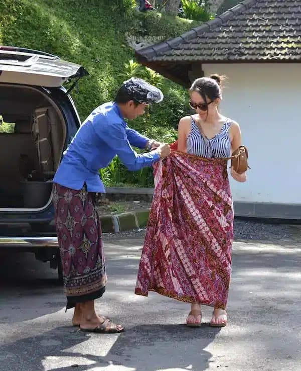 Things to Avoid in Bali - A guide teaches a tourist how to use a kamen or sarong