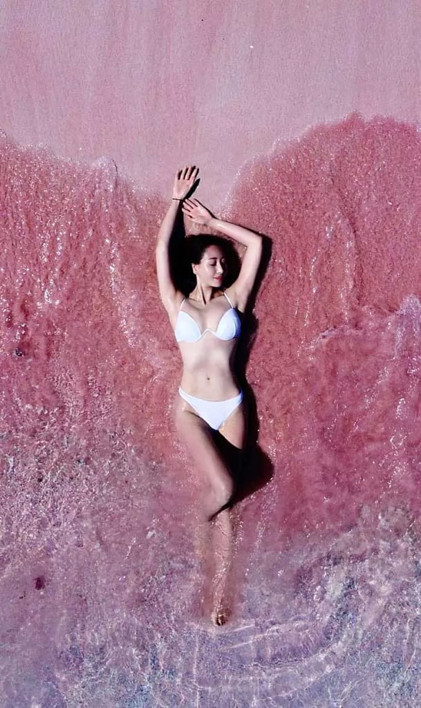 Aerial drone photo of woman sleeping on Pink Beach Komodo Island – pastel pink sand and turquoise water from above