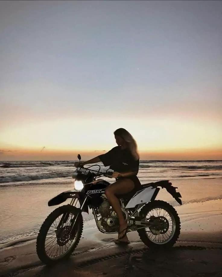 Adventurous blonde woman riding Honda CRF150 trail bike on Bali beach at sunset - rugged manual scooter rental for off-road exploration