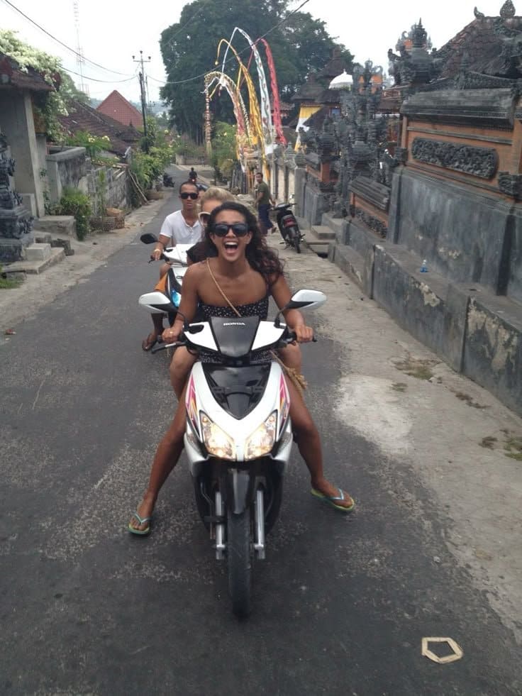 Two tourist women laughing on scooter after minor accident in Bali - positive perspective on travel mishaps