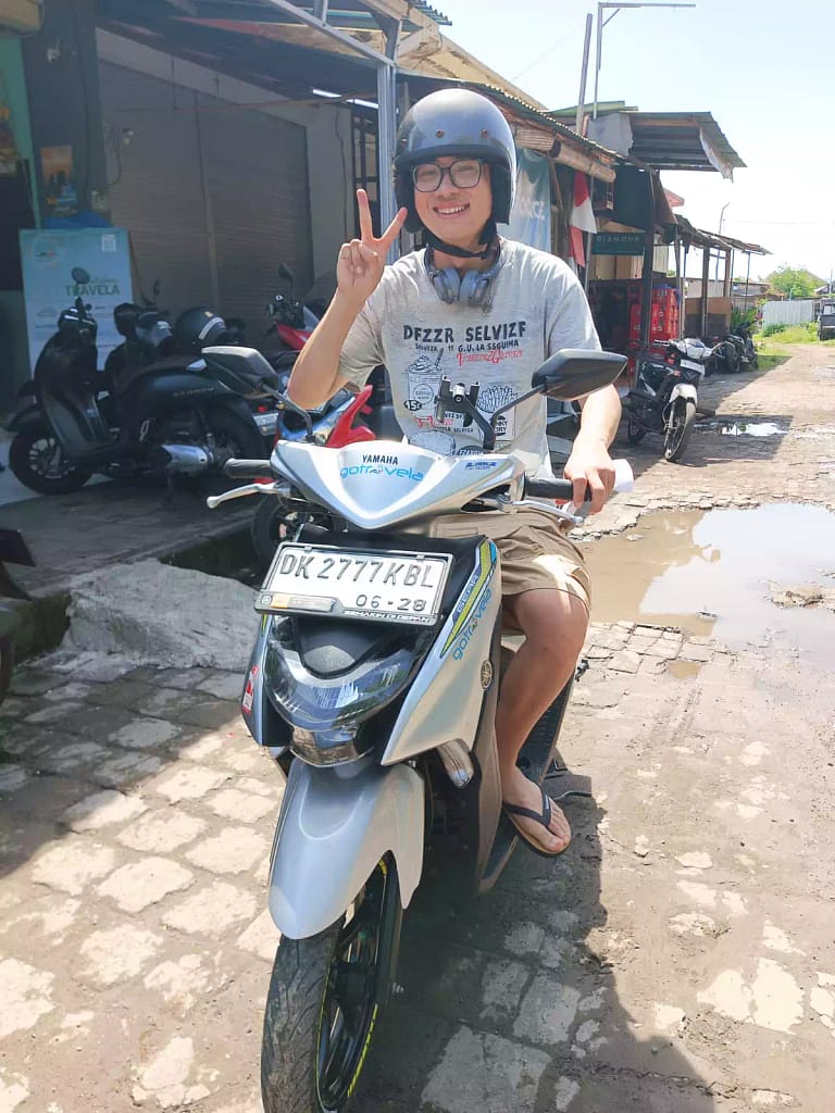Rent Scooter In Bali - Joyful tourist wearing helmet giving peace sign on rented scooter at Hey Bali Rental in Kuta - affordable motorbike hire with safety gear