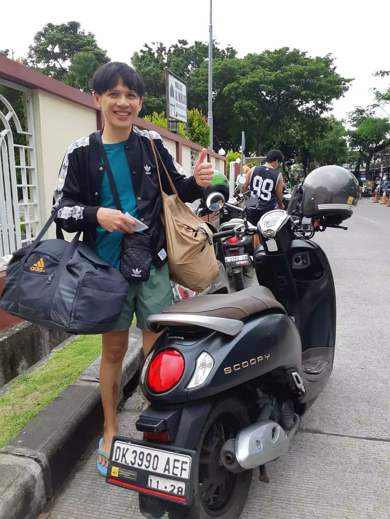 Scooter Bali Rental - Happy tourist standing with rented pink Honda Scoopy scooter at Bali airport parking - easy automatic motorbike rental for beginners - scoppy 110cc 2024 model - best for rent scooter in kuta bali