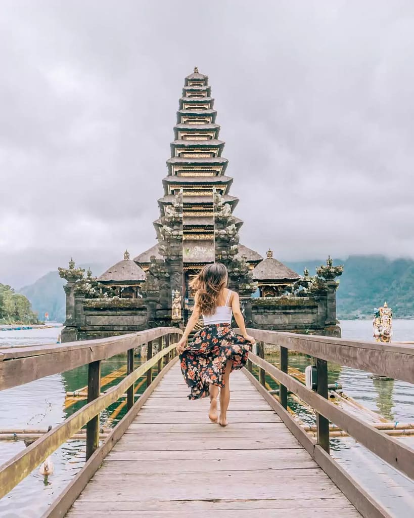 photo of a female tourist posing running on the bridge to the batur temple with a view of the lake batur in bali  