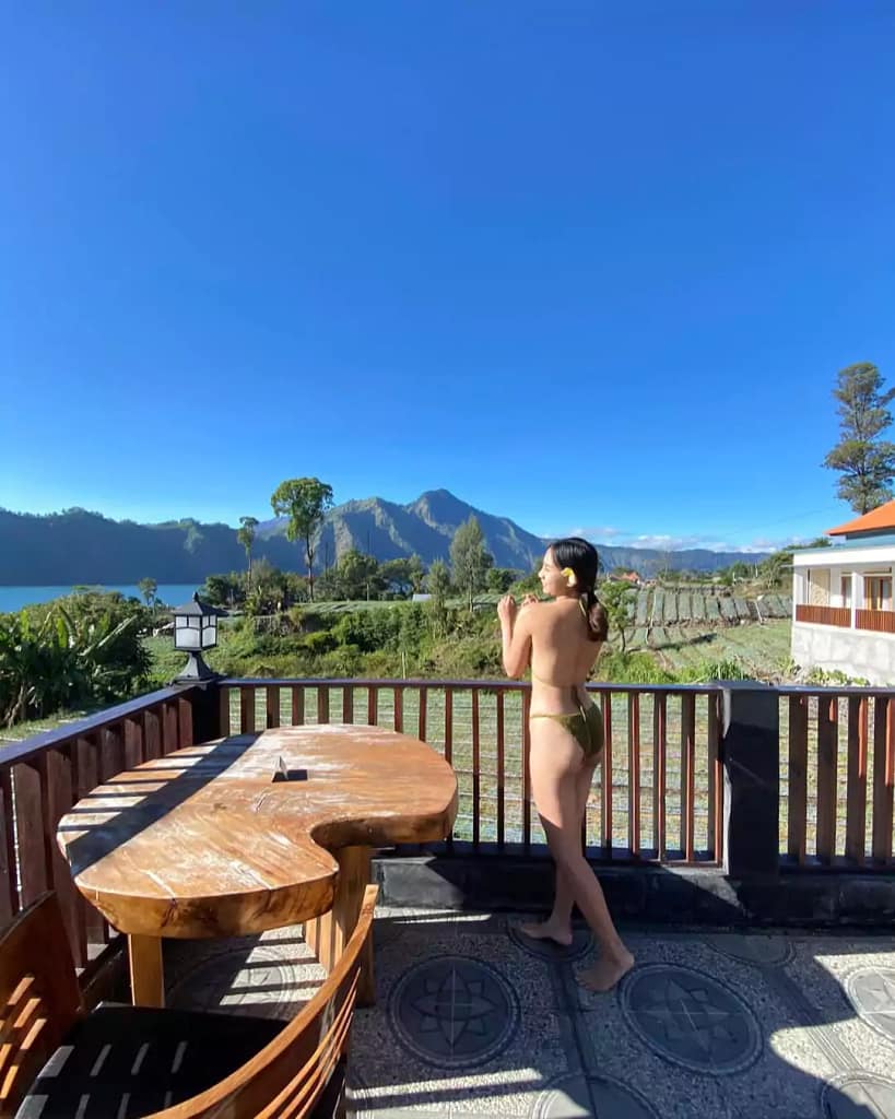a woman in a green bikini looks at Mount Batur and the lake in the bright morning weather and blue sky