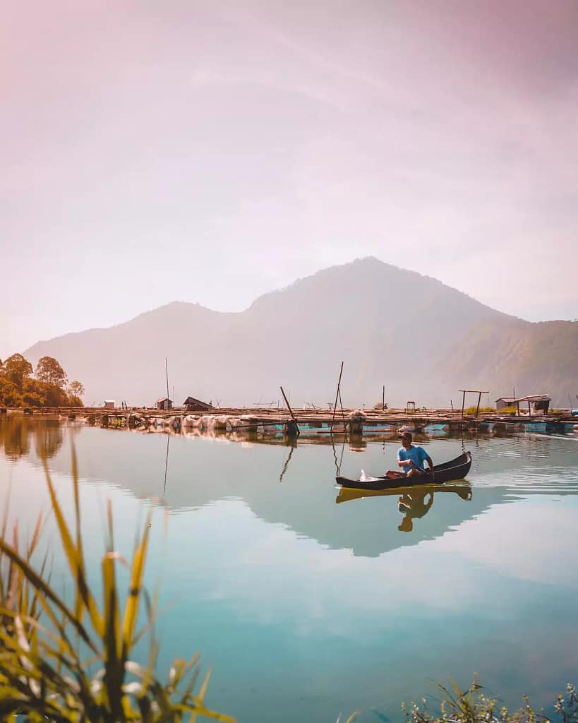 a man who is a tourist is paddling a traditional boat to fish in the middle of Lake Batur in Bali.