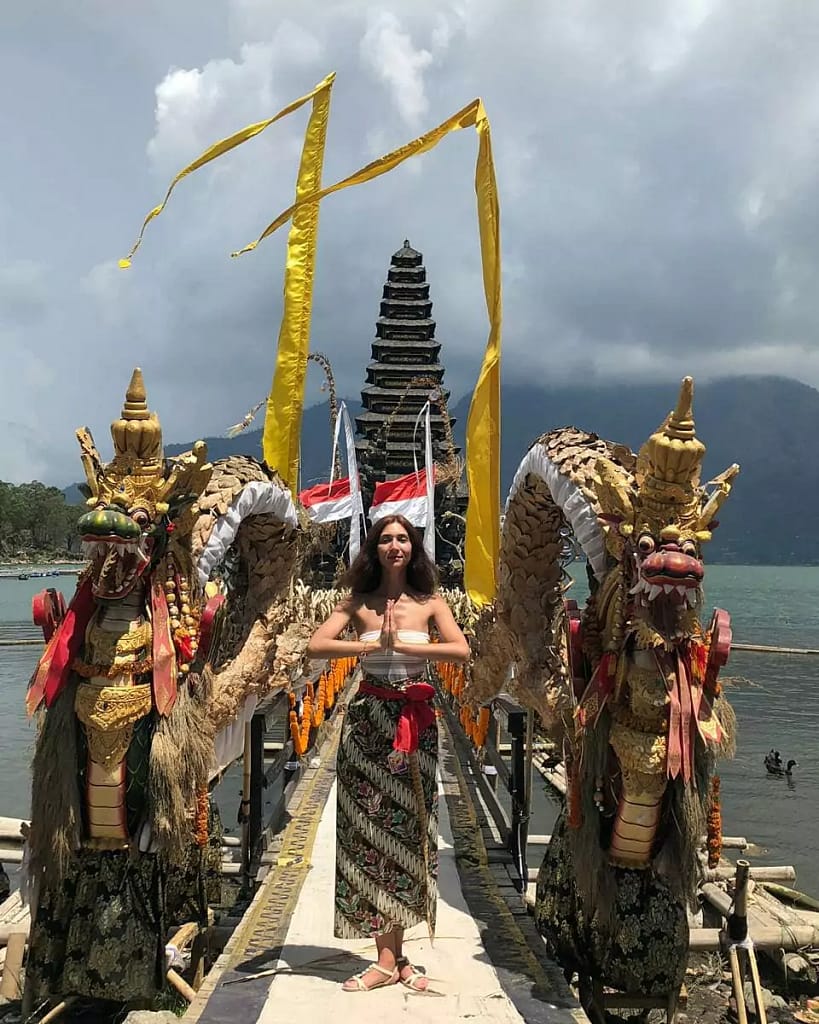 photo of a tourist from the Netherlands who is fully dressed and wearing a sarong and shawl taking pictures at the ulun danu batur kintamani temple
