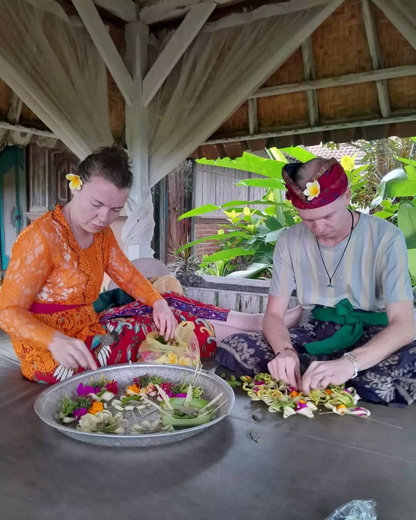 a couple of hey bali guests are learning to make canang sari by wearing full bali traditional clothes. - bali hindu offerings