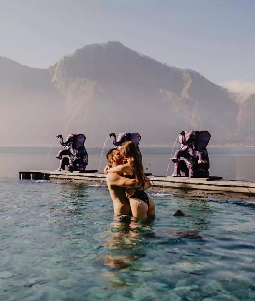 a couple of foreign tourists soaking while kissing in a hot spring pool with a view of the mountain and lake batur in bali