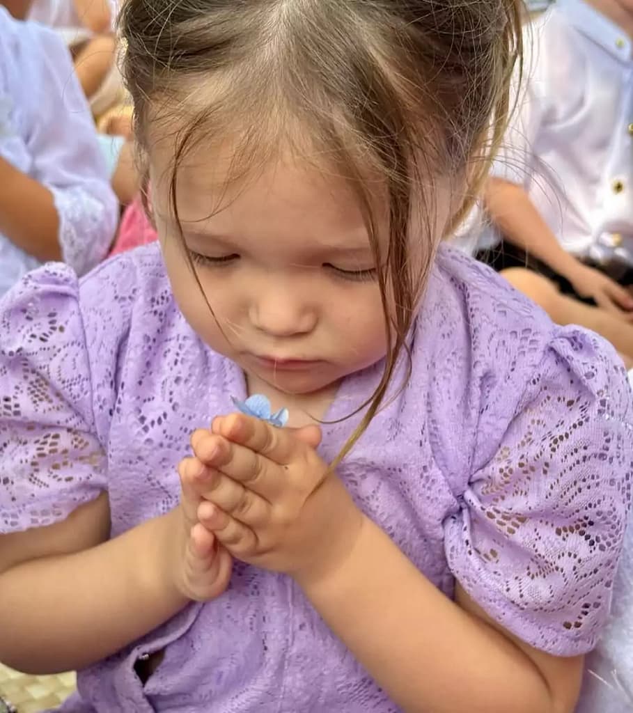 photo of a 3-year-old Caucasian child (woman) wearing full Balinese traditional clothes closing her eyes and both hands on her chest (sembah) looks very solemn praying