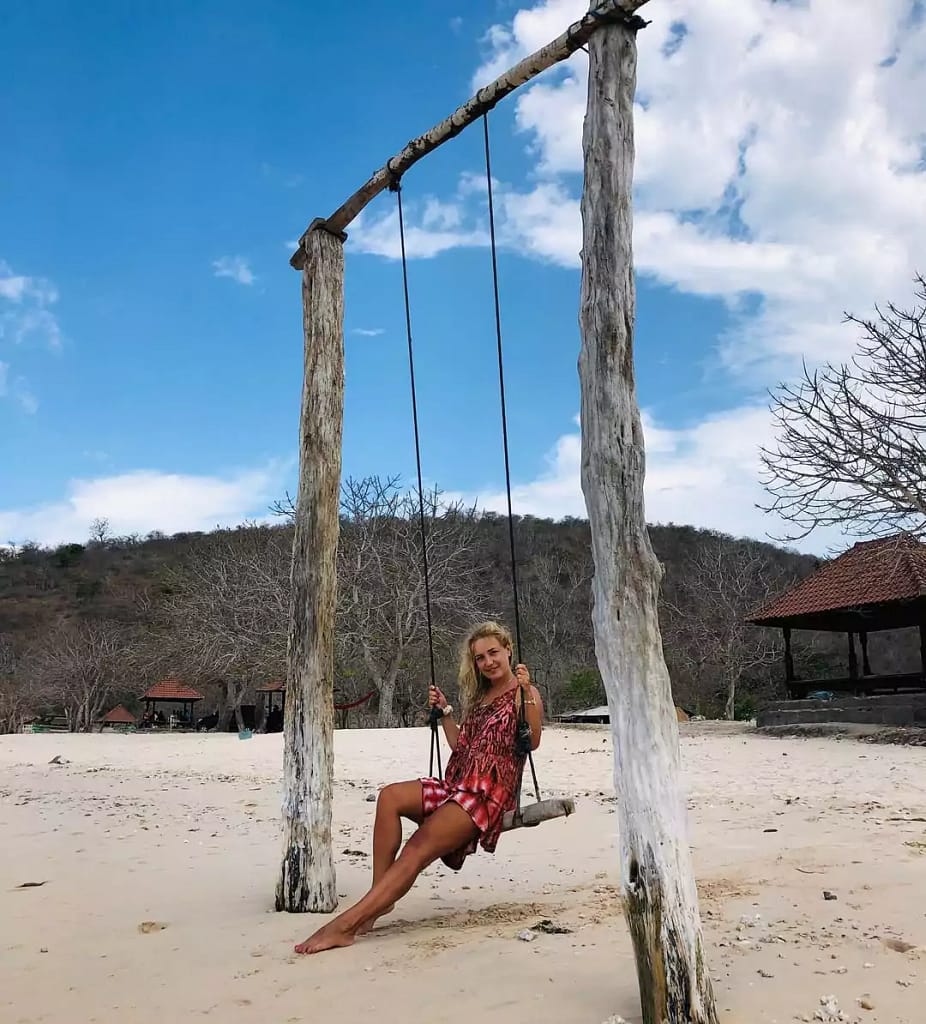 a woman on a swing at lombok pink beach in the afternoon 