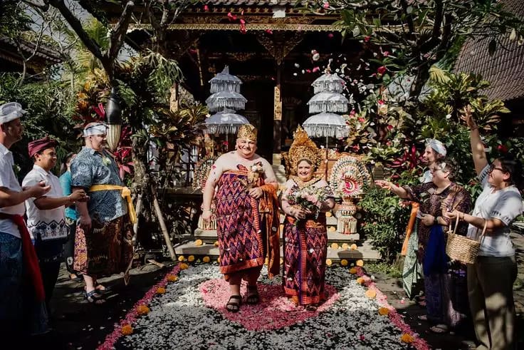 photo of the bule bride and groom wearing luxurious bali traditional clothes walking and being showered with flowers by their guests and relatives at a hotel in bali