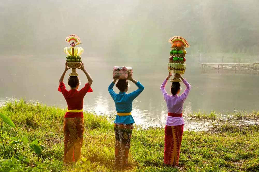 3 Balinese women wearing traditional clothes are carrying offerings on the edge of Lake Batur in Bali to honor the goddess Danu.