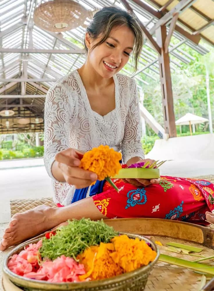 photo of a woman arranging flower arrangements in a canang sari to match the required position according to color and cardinal direction