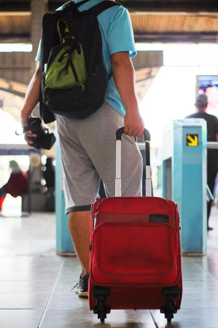 Traveler carrying red luggage and camera at a train station platform
