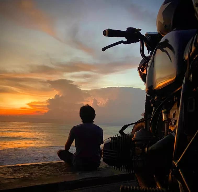 Man sitting on a wall next to his vintage motorcycle, watching the stunning ocean sunset over the horizon - Beaches in Tabanan for Sunset