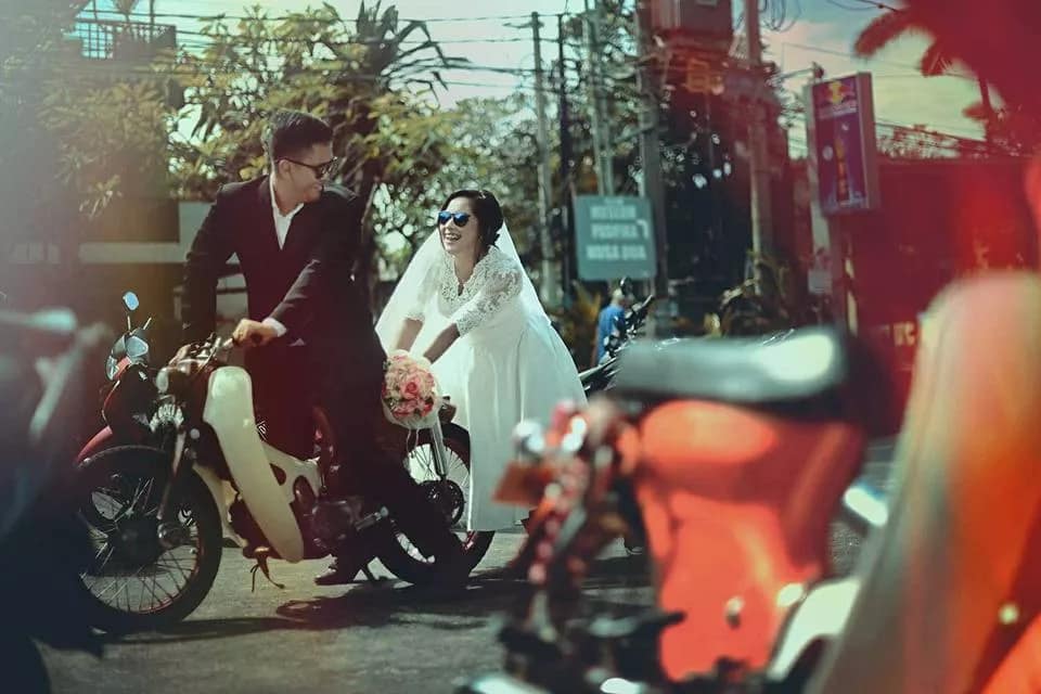 Photo with a funny concept, a bridal couple is pushing a broken down motorbike on the streets of Bali